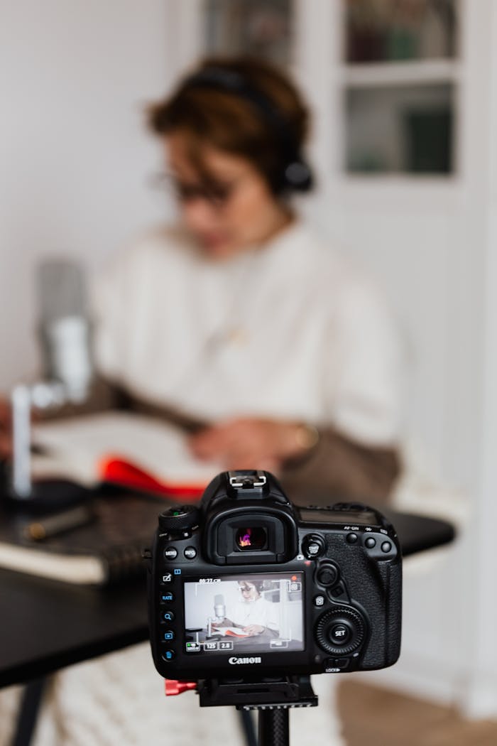 A Canon DSLR records a person with headphones reading and journaling.